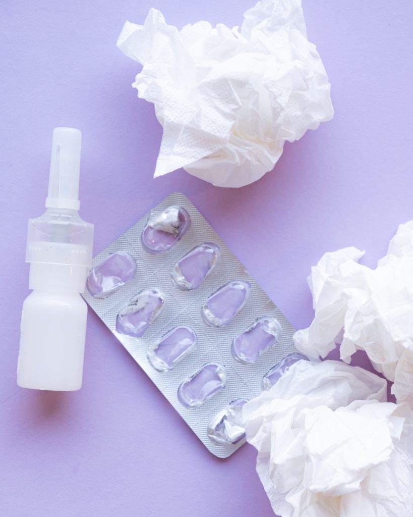 Tyhjä lääkeliuska, nenäsuihkepullo ja käytettyjä nenäliinoja